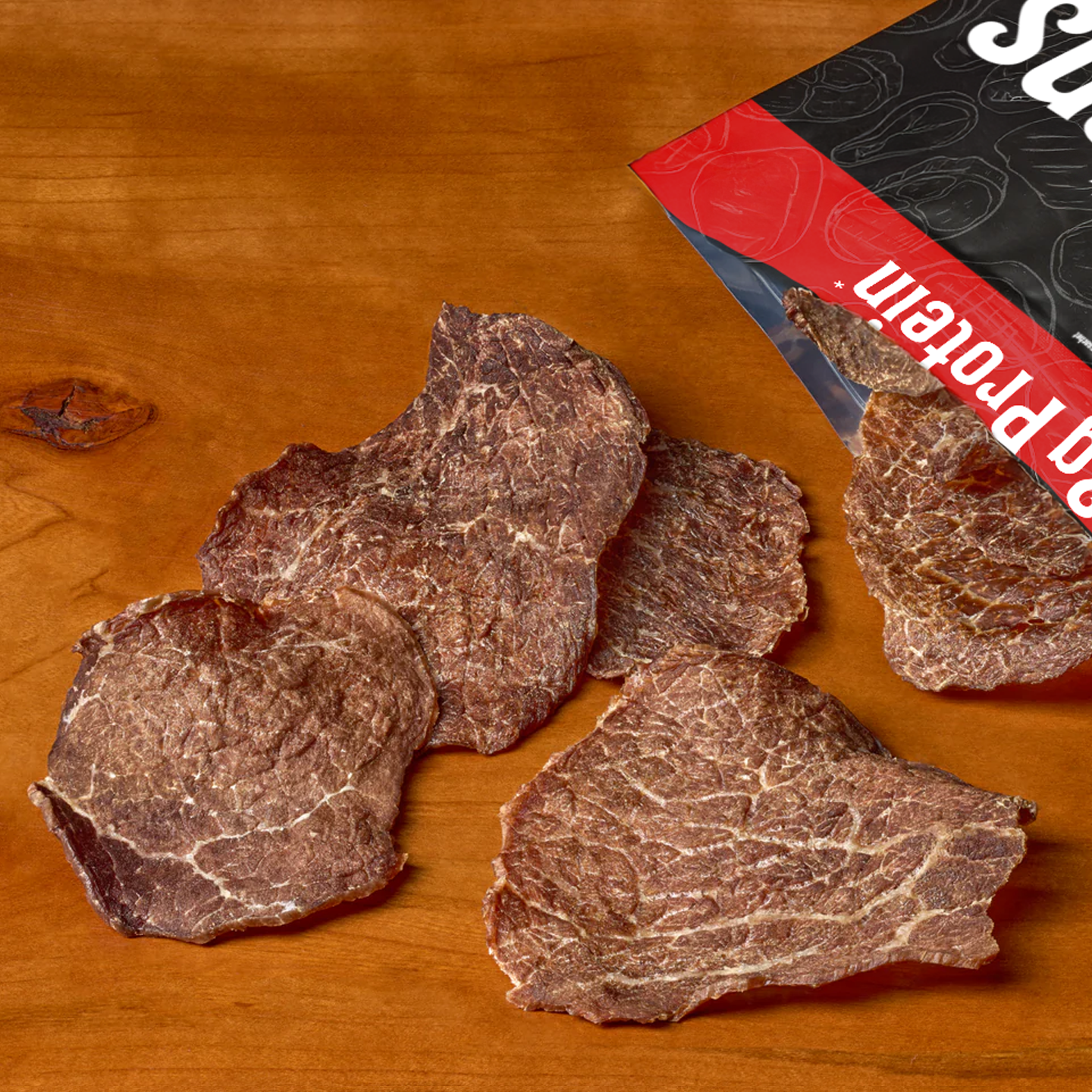 Beef Crisps beef jerky chips spilling out of bag onto wooden surface showing thin crispy texture